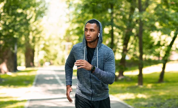 Millennial corredor com fones de ouvido desfrutando de sua corrida matinal no parque de verão, espaço vazio — Fotografia de Stock