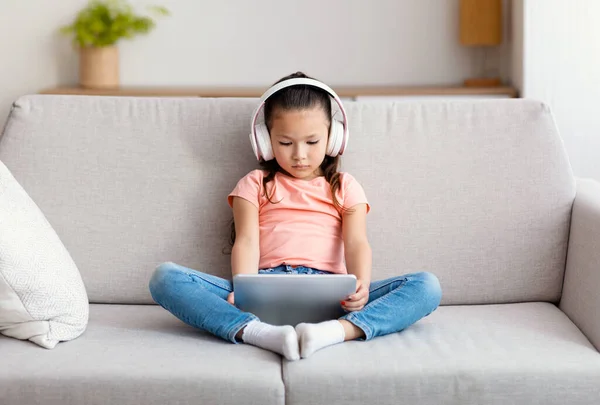 Menina usando tablet digital e fones de ouvido assistindo desenhos animados sentados dentro — Fotografia de Stock