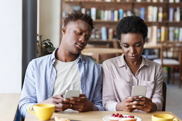 Problema de phubbing. casal preto preso em seus smartphones em data chata no café — Fotografia de Stock