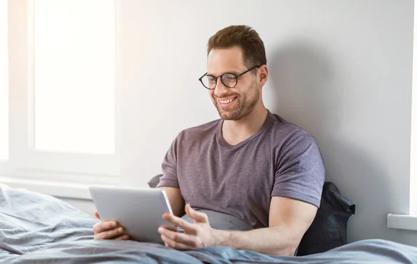Happy Man Korzystanie z tabletu Przeglądanie Internetu Siedząc w łóżku w domu — Zdjęcie stockowe