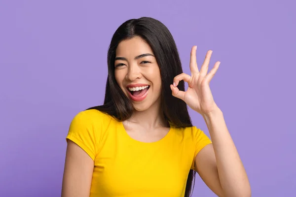Va tutto alla grande. Gioioso asiatico donna mostrando ok segno oltre viola sfondo — Foto Stock