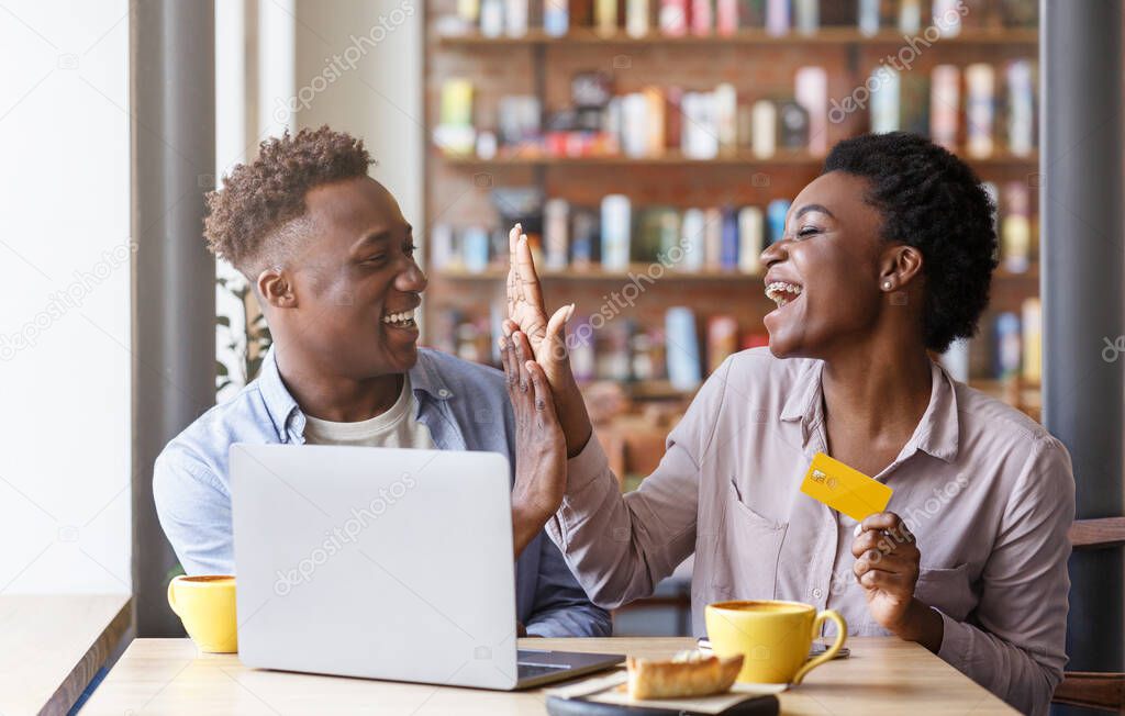 Online shopping. Millennial black couple with credit card making high five gesture near laptop at cafe