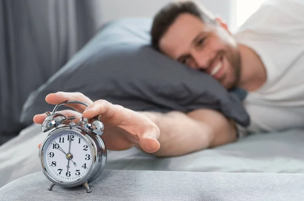 Щасливий чоловік вимикає сигналізацію-годинник встає в ліжку в приміщенні — стокове фото