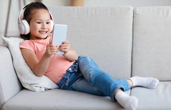 Menina usando telefone jogar jogo móvel deitado no sofá interior — Fotografia de Stock