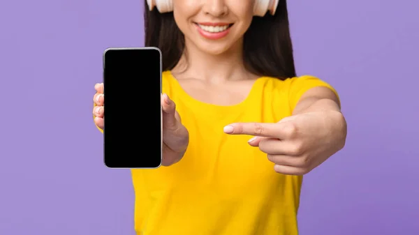 Scarica musica online. Ragazza irriconoscibile in cuffie che indica sullo schermo dello smartphone nero — Foto Stock