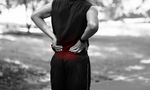 Şehir parkındaki eğitimde sırtında ağrı hisseden genç bir adamın görüntüsü, siyah beyaz etkisi. — Stok fotoğraf
