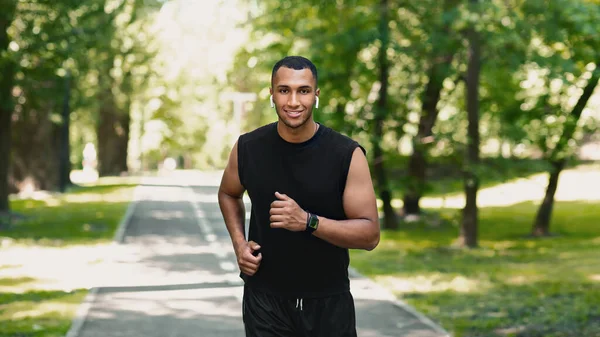 Sonriente joven corredor de entrenamiento en pista de jogging en hermoso parque verde —  Fotos de Stock