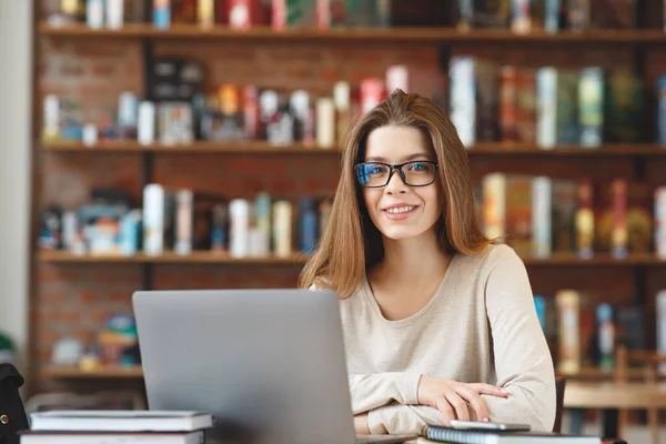 Menina sorridente em óculos relaxando no café e usando computador portátil — Fotografia de Stock