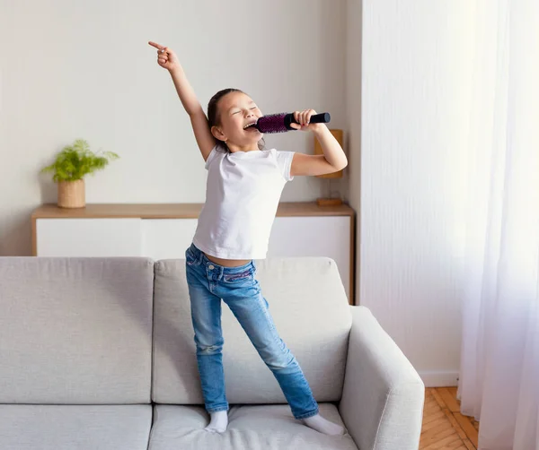 Girl Singing Holding Hairbrush Like Microphone Standing On Sofa Indoor — Stok Foto