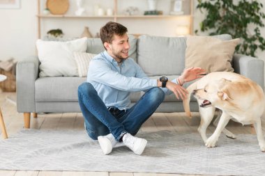 Yakışıklı bir adam oturma odasında köpeğiyle oynuyor.