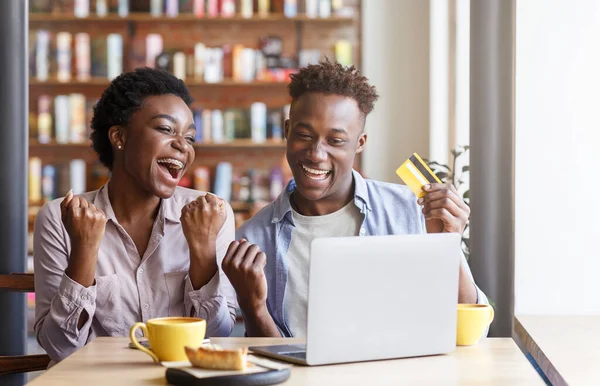 Feliz pareja negra con tarjeta de crédito y ordenador portátil de compras en línea en la cafetería — Foto de Stock