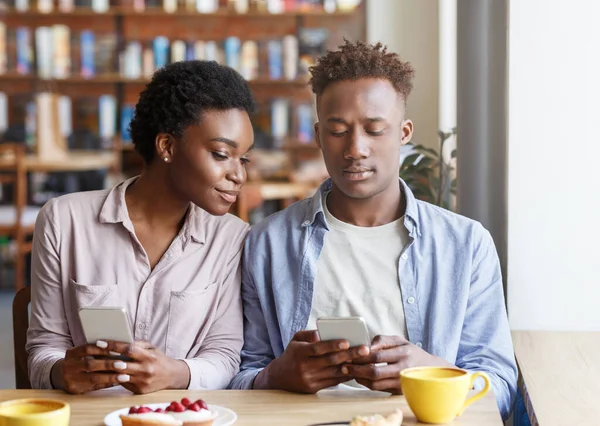 Uzależnienie od Internetu. Millennial czarny facet i dziewczyna patrząc na telefony komórkowe na nudną randkę w kawiarni — Zdjęcie stockowe