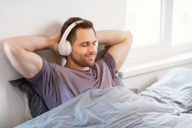 Kulaklıkla müzik dinleyen, yatakta dinlenen bir adam.