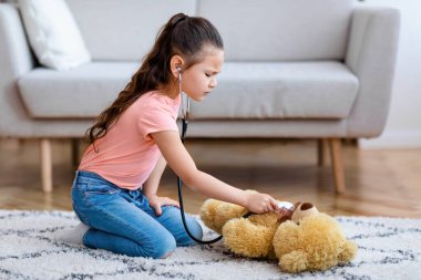 Küçük Çinli kız evde oyuncak ayıyla doktorculuk oynuyor.