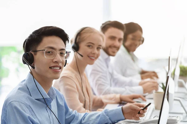Trabalhadores sorrindo do call center sentados na fila perto de seus computadores no escritório claro, espaço em branco — Fotografia de Stock