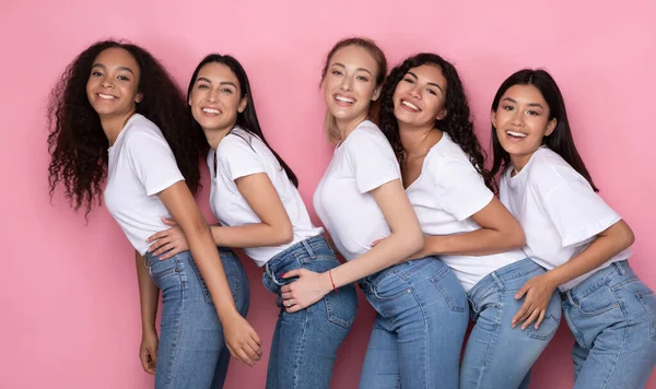 Cinco mulheres multirraciais abraçando posando no fundo do estúdio rosa — Fotografia de Stock