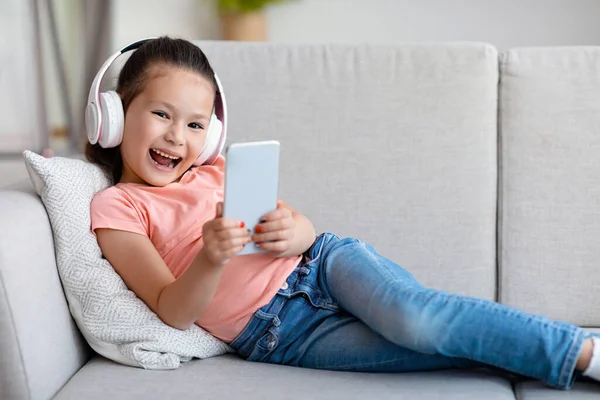 Ragazza bambino eccitato utilizzando Smartphone sdraiato sul divano a casa — Foto Stock