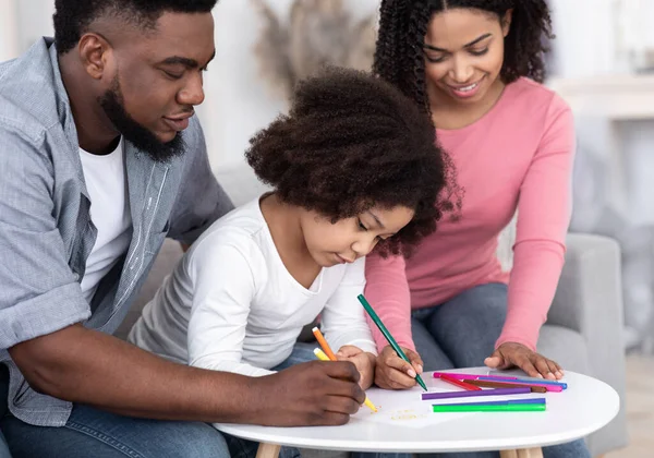 Zorgzame Afro-Amerikaanse ouders onderwijzen hun kleine dochter tekenen thuis — Stockfoto