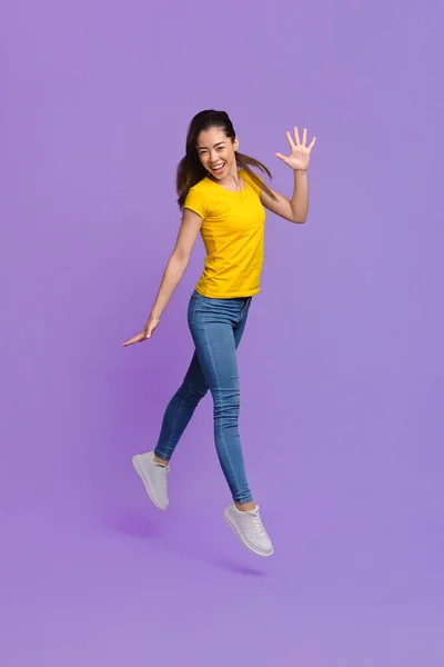 젊음의 즐거움. 찬란 한 배경을 두고 공중으로 뛰어오르는 쾌활 한 아시아 소녀 — 스톡 사진