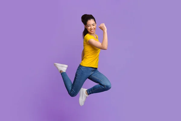 Joie asiatique fille saut avec levé poings sur pourpre studio fond — Photo