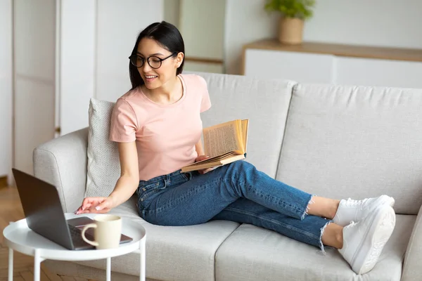 Студентка с ноутбука и чтение книги сидит дома — стоковое фото