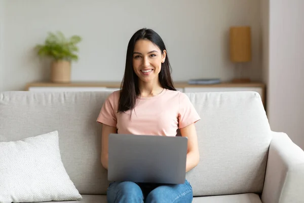 Ragazza allegra seduta con il computer portatile sul divano che lavora da casa — Foto Stock