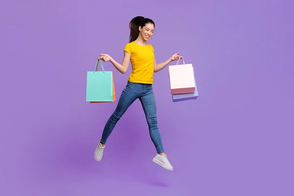 Счастливого шоппинга. Радостная азиатская девочка прыгает в воздухе с огромными сумками для покупок — стоковое фото