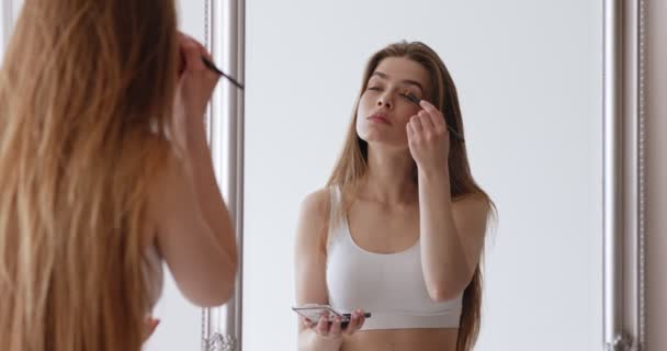 Jeune femme regardant miroir et appliquant des fards à paupières — Video