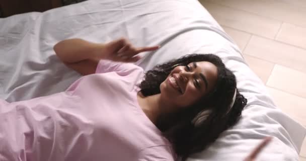 Glad afrikansk amerikansk flicka njuter av favoritmusik i sängen — Stockvideo