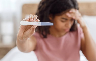 Pozitif hamilelik testi tutan üzgün zenci kadın.