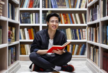 Kütüphanede kitap okuyan gülümseyen Çinli adam.