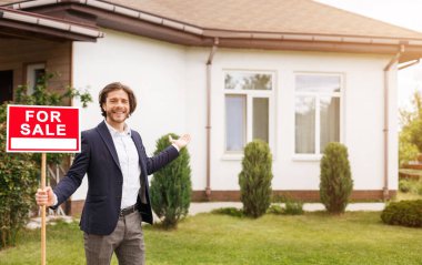 Açık havada güzel bir evi gösteren satılık tabelası olan neşeli bir emlakçı. Boş boşluk