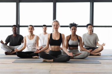 Lotus pozisyonunda oturmuş birlikte meditasyon yapan çok kültürlü gençlerden oluşan bir grup.