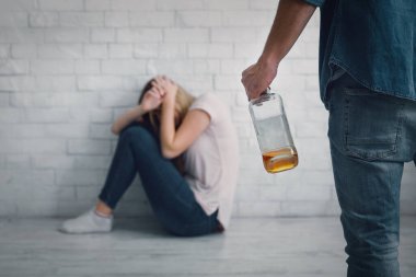 Agresif alkolik mağduruna yardım. Kadın, elinde şişeyle kendini kocasını yumruklamaya kapatıyor.