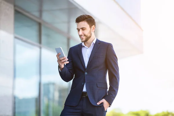 Empresario joven exitoso usando el teléfono celular para la comunicación en línea cerca de la oficina del gobierno — Foto de Stock