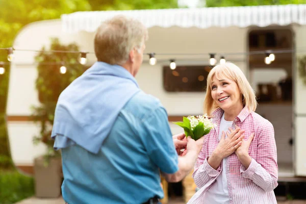 Cuidar hombre mayor dando ramo de flores de campo a la esposa cerca de RV fuera — Foto de Stock