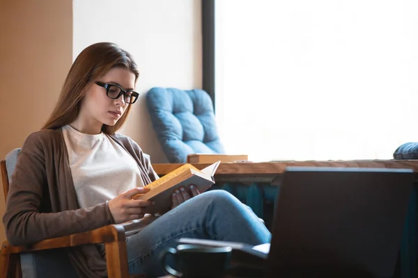 Jonge vrouw leest interessant boek en zit thuis — Stockfoto