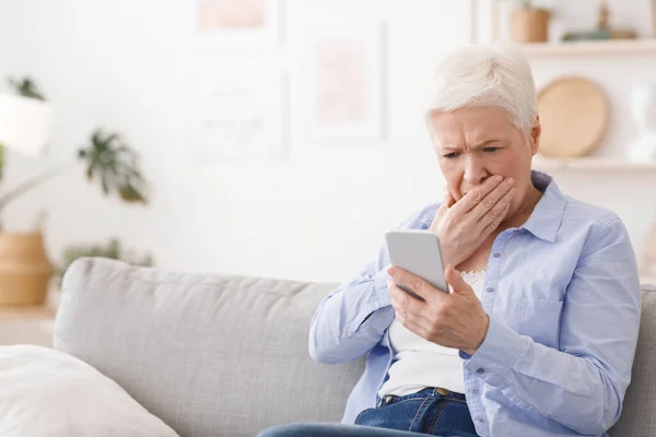 Ανησυχούσα ηλικιωμένη κυρία διαβάζοντας συγκλονιστικά νέα στο smartphone στο σπίτι — Φωτογραφία Αρχείου