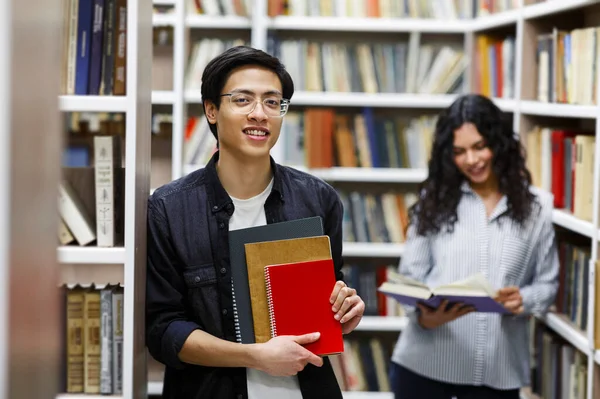 Sorrindo coreano cara segurando livros didáticos na biblioteca do campus — Fotografia de Stock