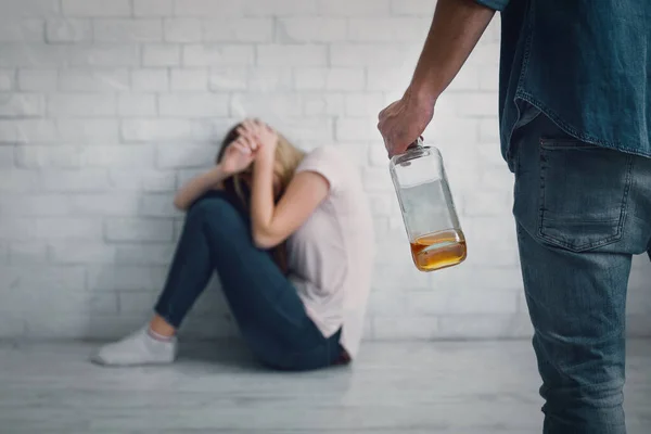 Ajuda para vítima de alcoolismo agressivo. Esposa se fecha de golpes de marido, com garrafa na mão — Fotografia de Stock