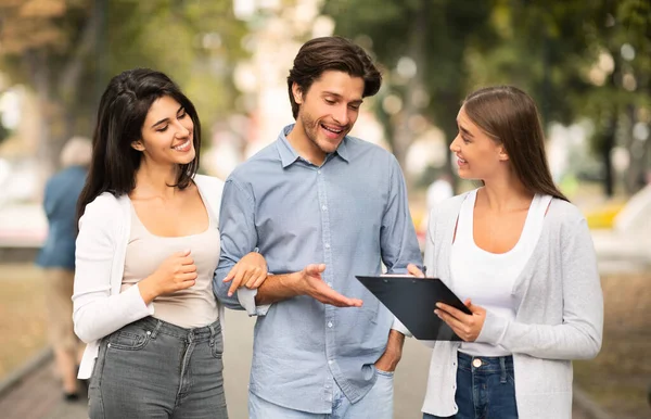 Menina entrevistando jovem casal realizando levantamento sociológico em pé ao ar livre — Fotografia de Stock