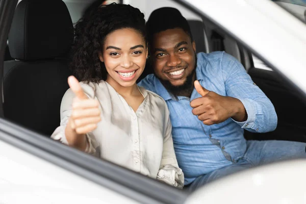 Радостная африканская пара с большими пальцами сидит в машине — стоковое фото