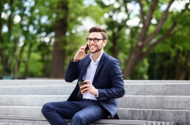 Parktaki taş merdivenlerde cep telefonuyla konuşan başarılı bir işyeri sahibi.