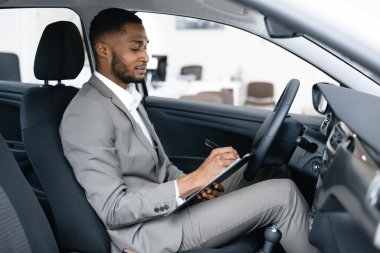 Dağıtıcı, otomobilleri kontrol ederken arabada otururken not alıyor.