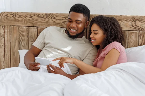 Cheerful couple using new mobile app, lying in bed — Stock Photo, Image