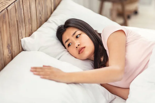 Frustrada mujer coreana tocando almohada vacía acostada en la cama interior —  Fotos de Stock