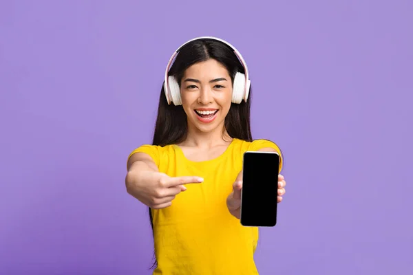 App musicale. joyeuse asiatique fille dans haadphones pointant sur noir Smartphone écran — Photo