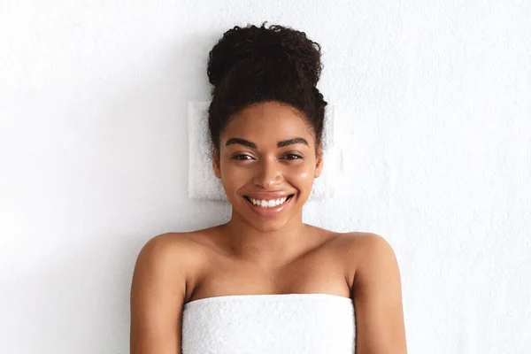 Vacker leende afrikansk flicka insvept i handduk liggande på vit — Stockfoto