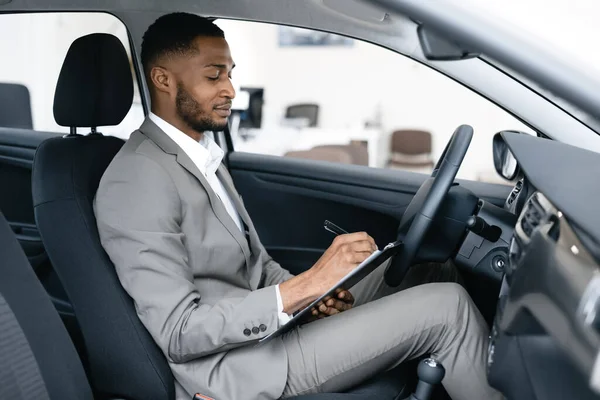 Negociante tomar notas sentado no carro verificando automóvel em Dealership — Fotografia de Stock