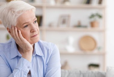 Üzgün, yaşlı bir kadının portresi. Evde oturuyor ve başka tarafa bakıyor.